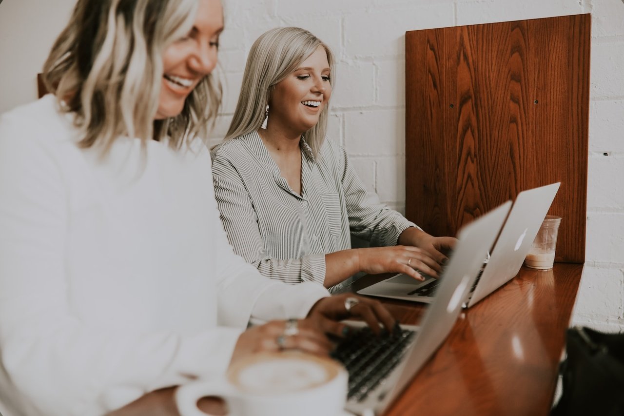 two women working with laptops and smiling