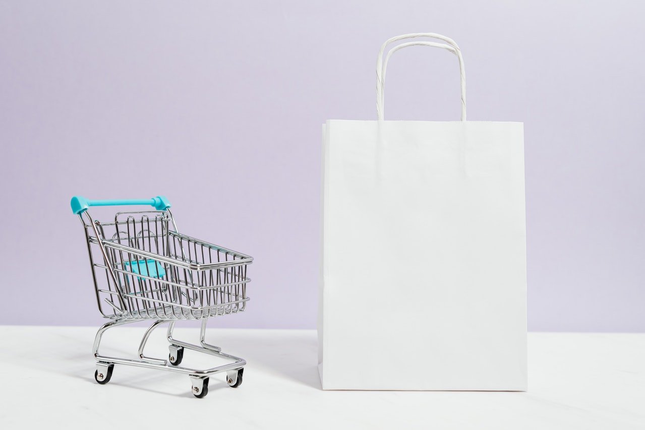 small shopping cart and a white shopping bag with a lilac background