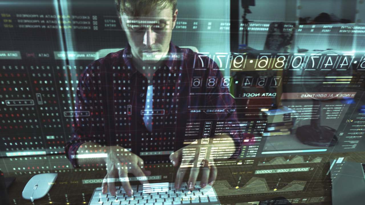 a man who is coding is reflected on the computer screen