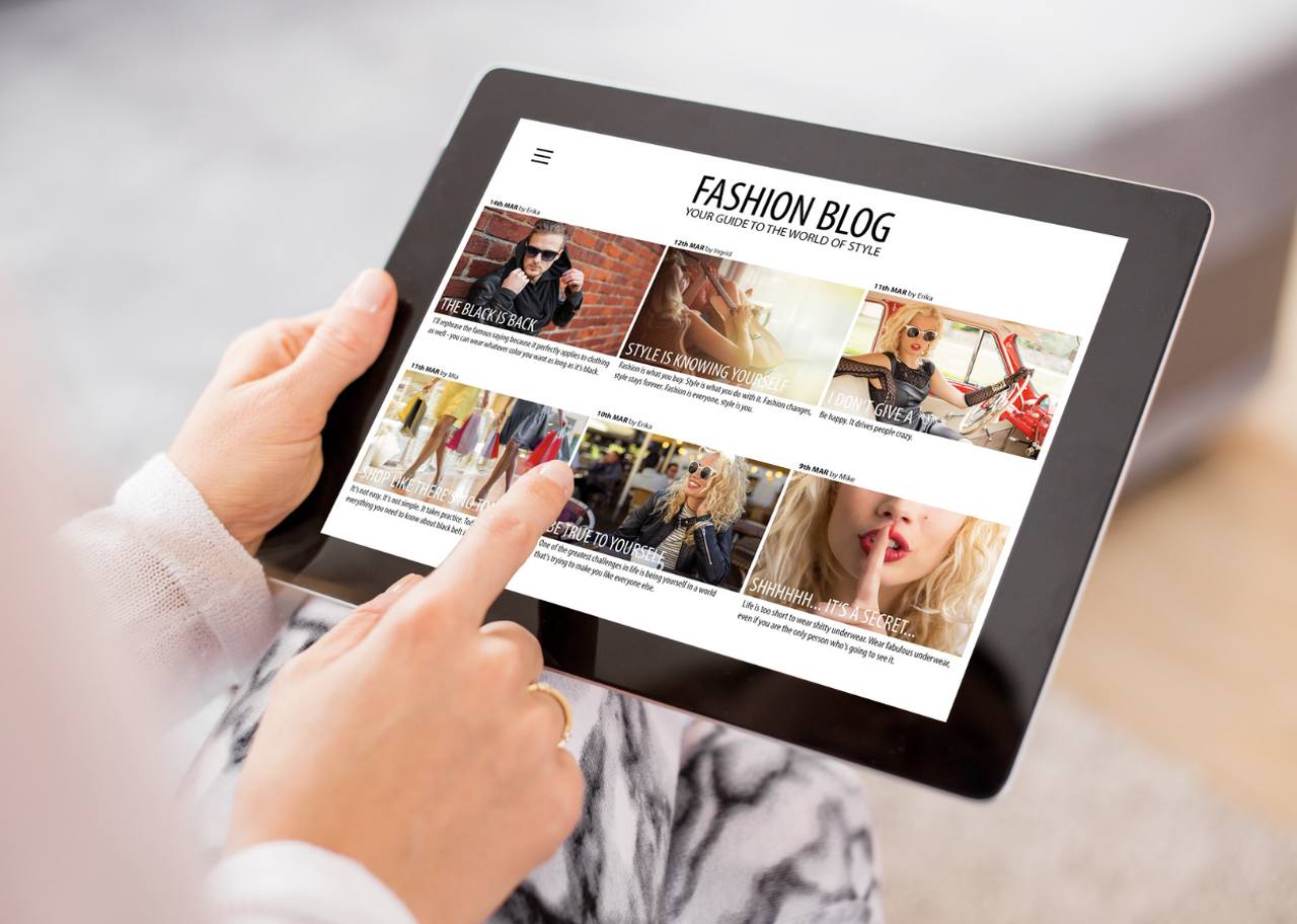 hands holding a tablet that is showing a fashion blog page with their cover images
