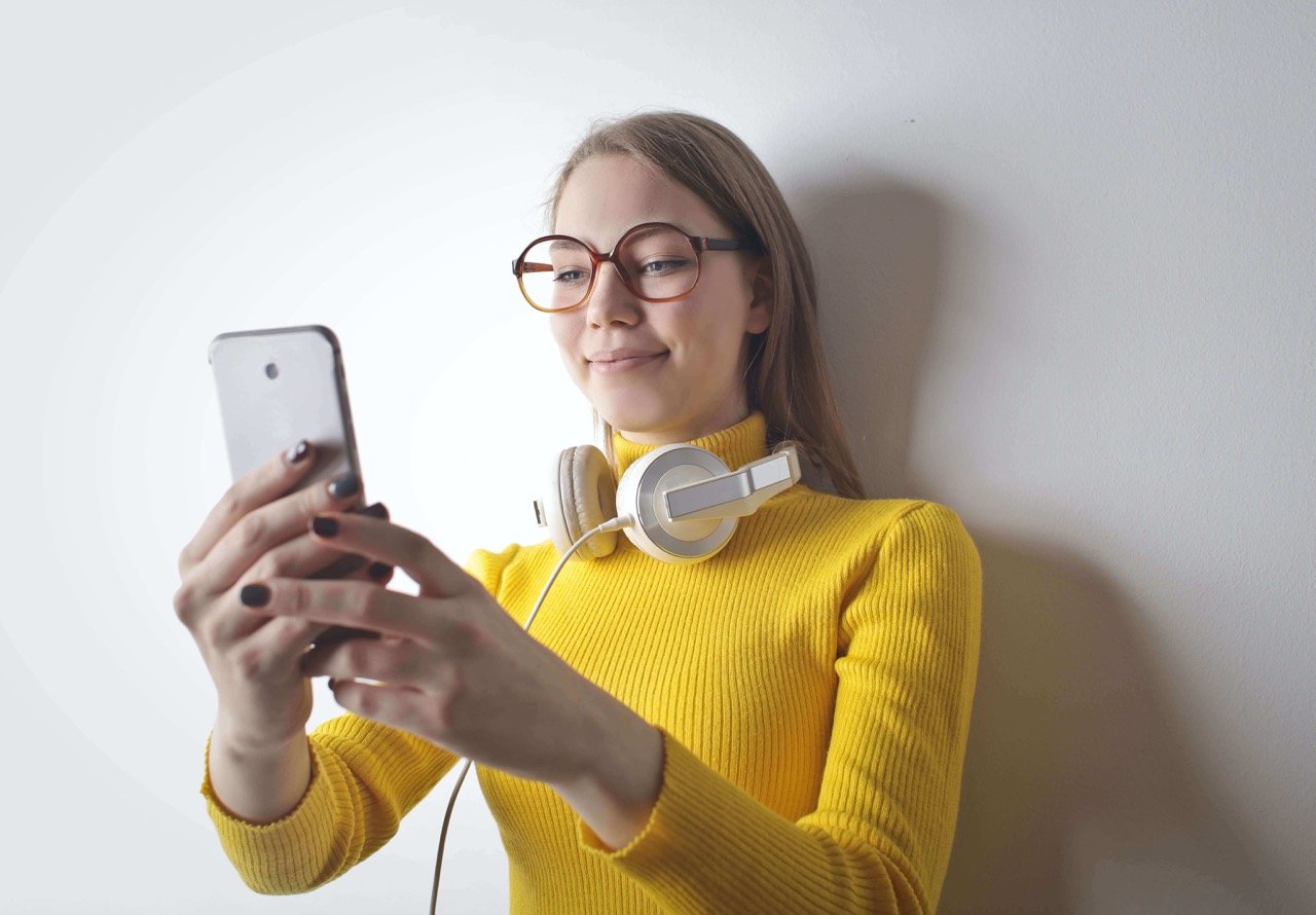 kulaklık takan ve telefonunu kontrol eden sarı boğazlı kazak giymiş kadın