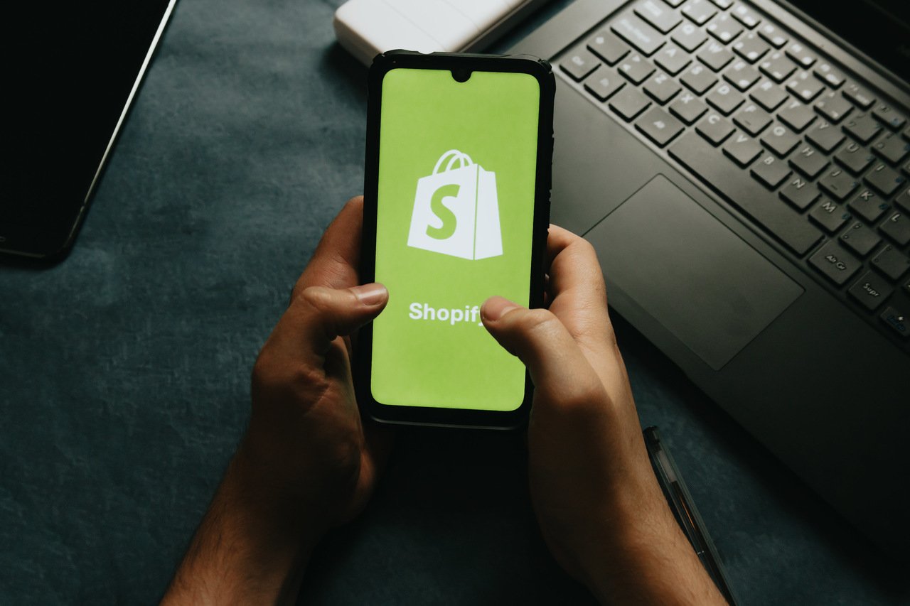 The Shopify app opening on a green screen on a smartphone held in the hands
