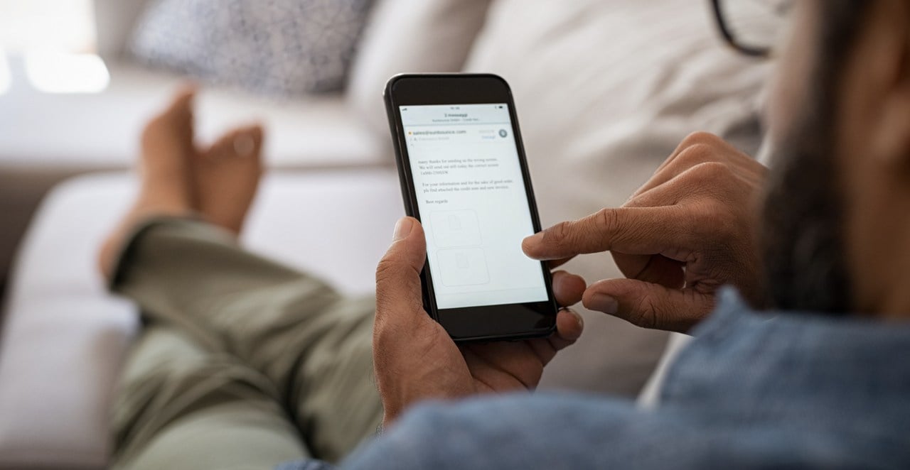 Person checking emails on a smartphone while laying on a couch with hands holding phone visible
