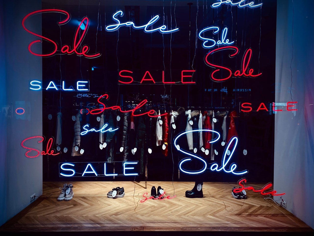 A store window displaying shoes with neon red and white lettering that says “Sale”