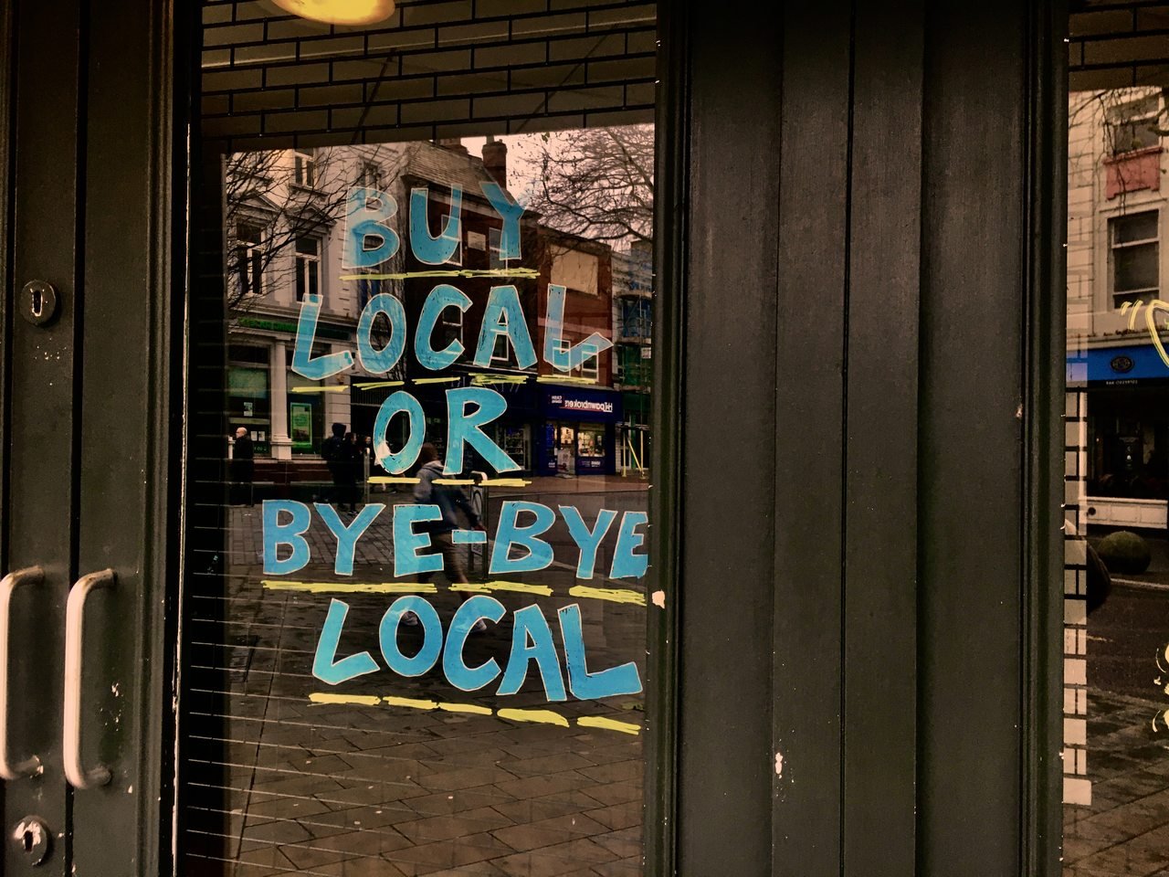A photo of a blue sign above a door that reads “Shop Local or Local Disappears”