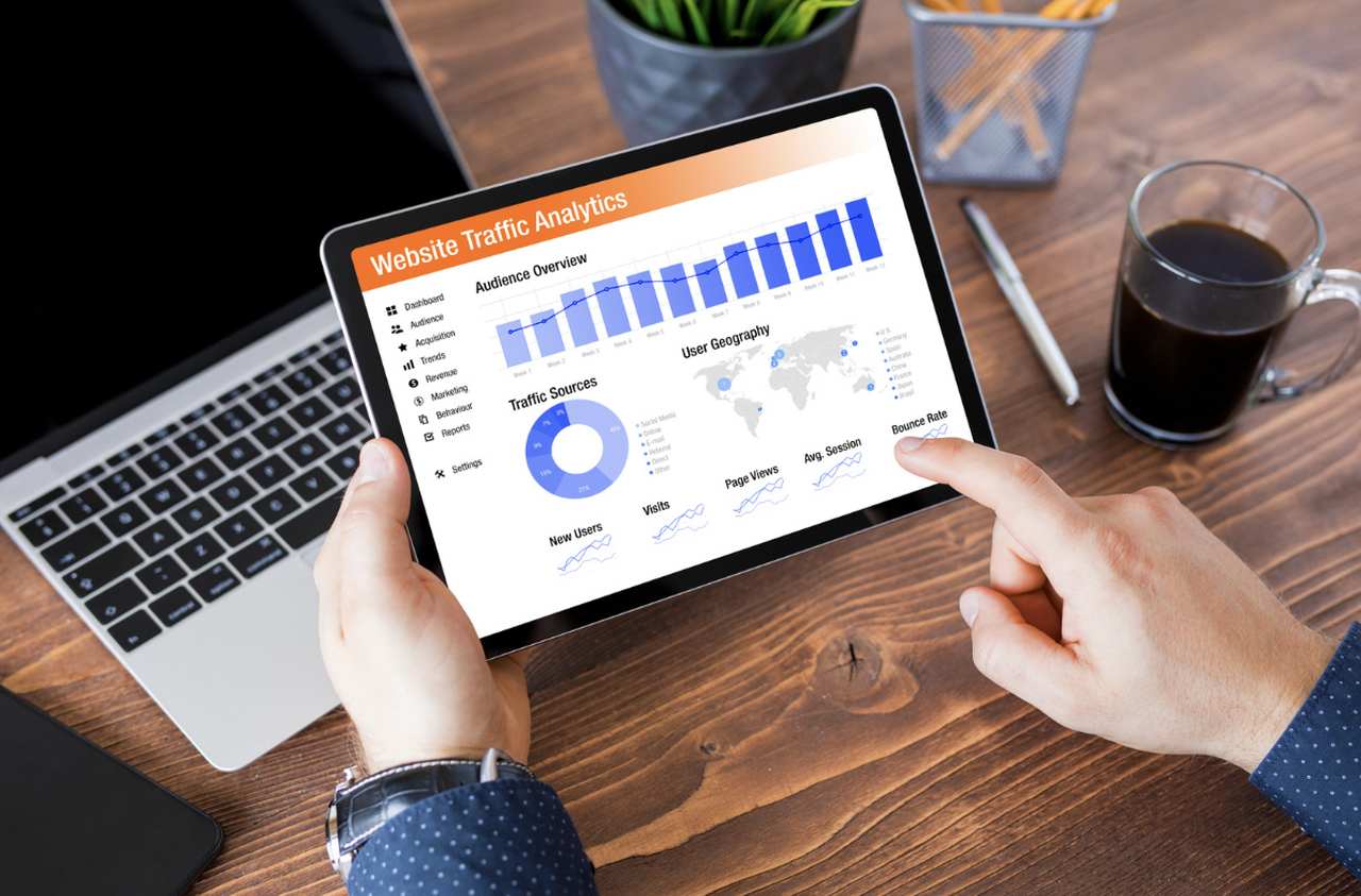 A man's hands using Google Analytics on a tablet and a coffee cup on the table