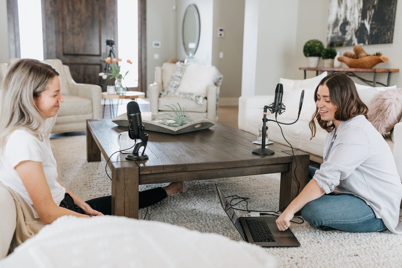 Two women recording a podcast together in a home studio setup