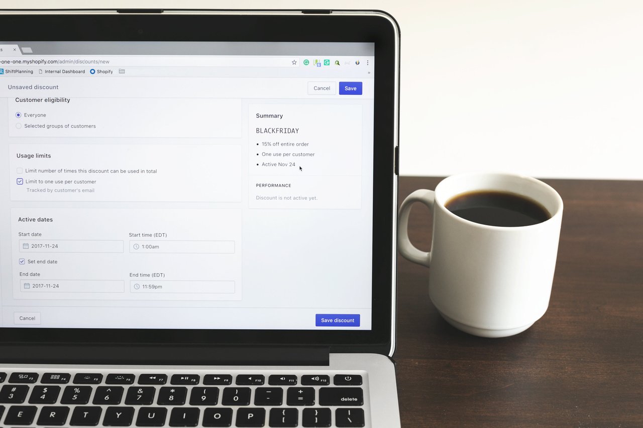 Shopify'de indirim kodu ayarlarını gösteren bir MacBook ve yanında bir fincan kahve