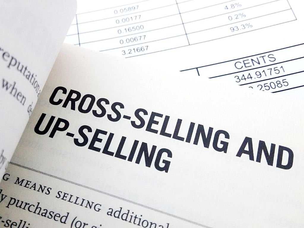 A close-up of a book showing the title “Cross-selling and up-selling” with a paper visible under it with some numbers on it