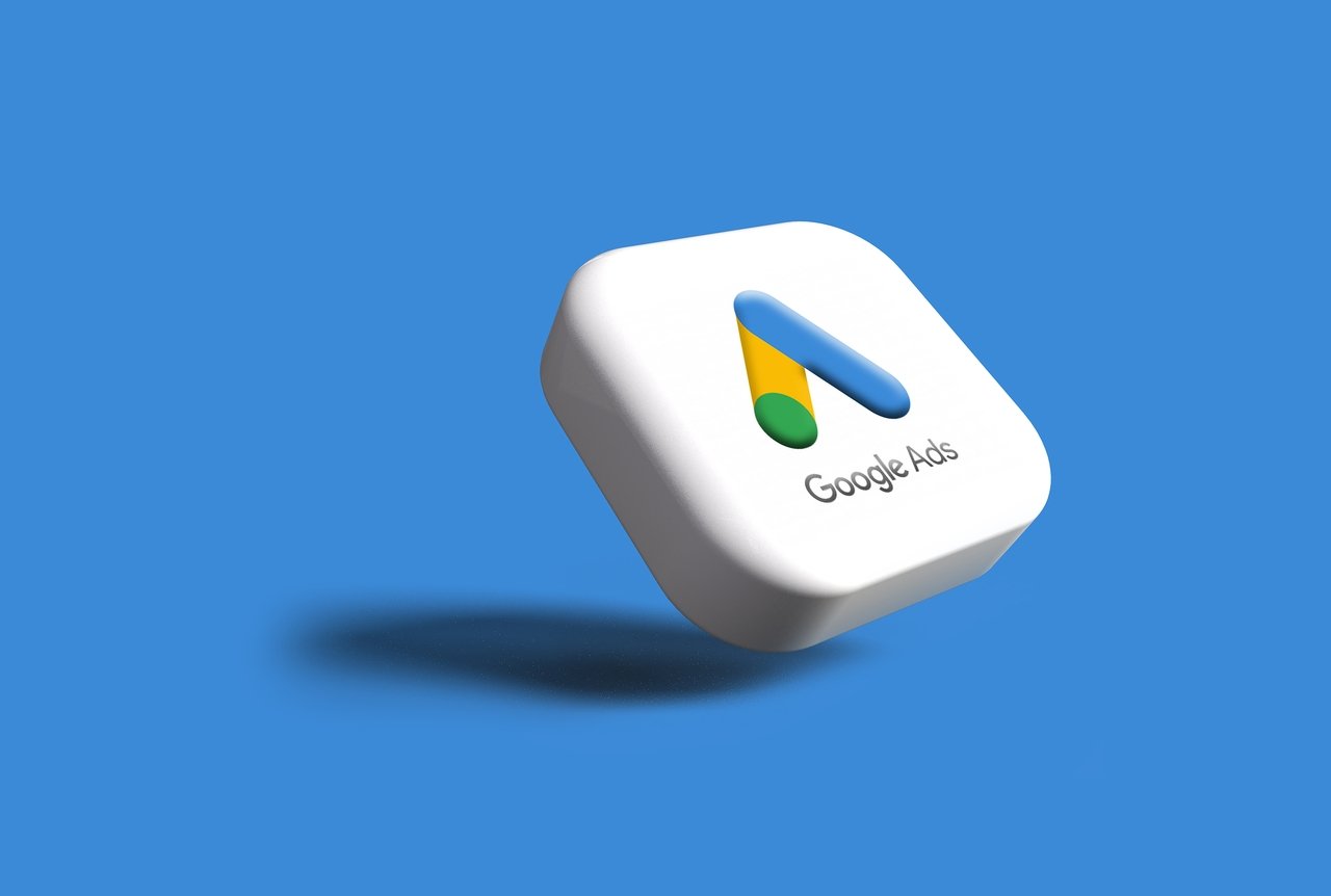 Google Ads stok görseli, beyaz bir kare içinde 3 boyutlu Google Ads logosunu ve gölgesini mavi bir arka planda gösteriyor