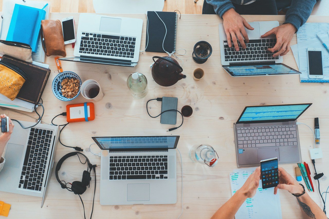 Laptoplar, kulaklıklar, yiyeceklerle dolu bir masa, bazı eller laptoplarda blog yazıları yazıyor