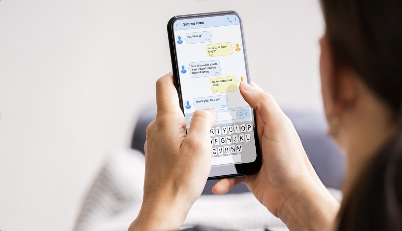 Person holding phone with both hands checking SMS messages with face partially visible