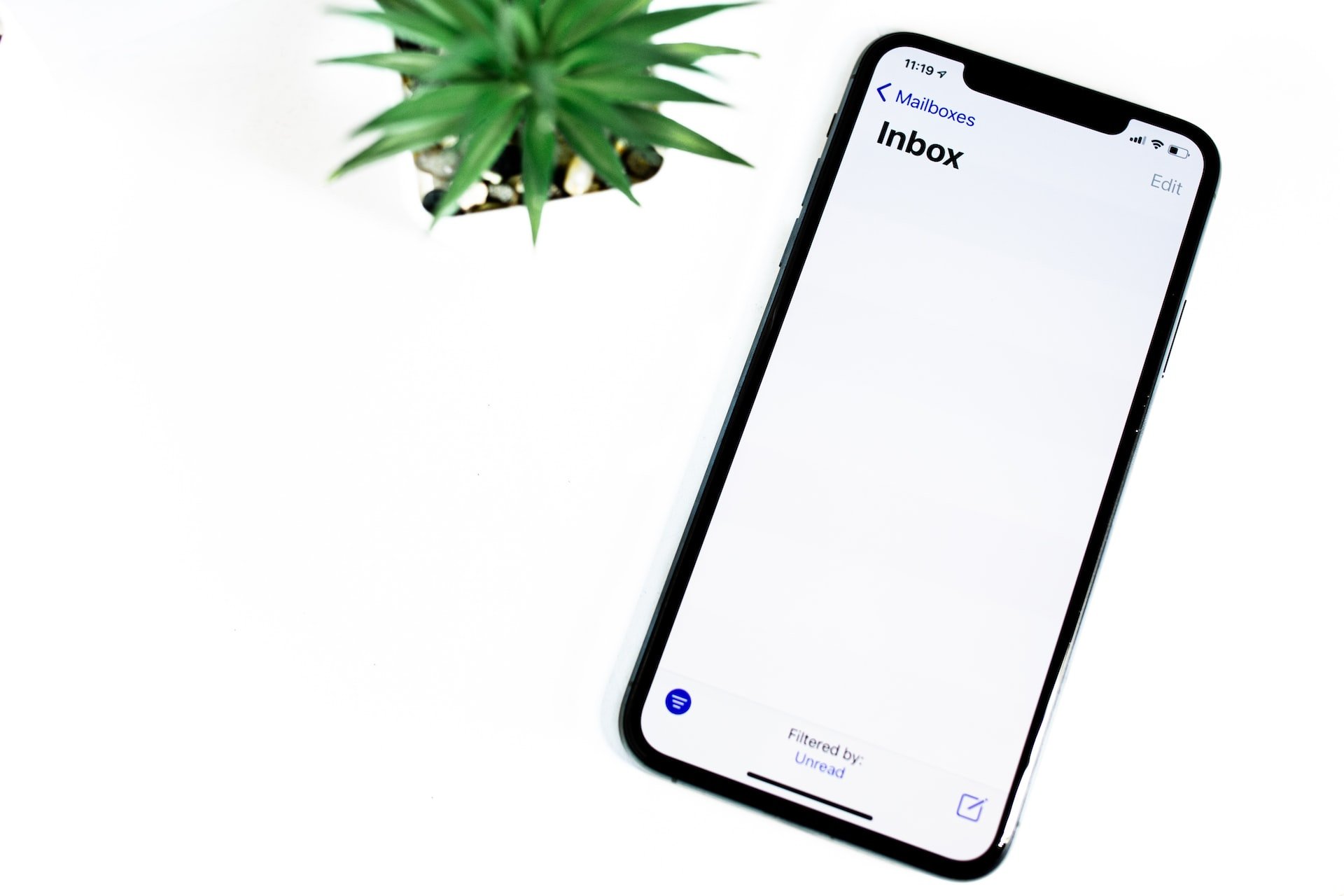 Beyaz bir masa üzerinde saksı bitkisinin yanında bir mobil telefonda boş e-posta gelen kutusu