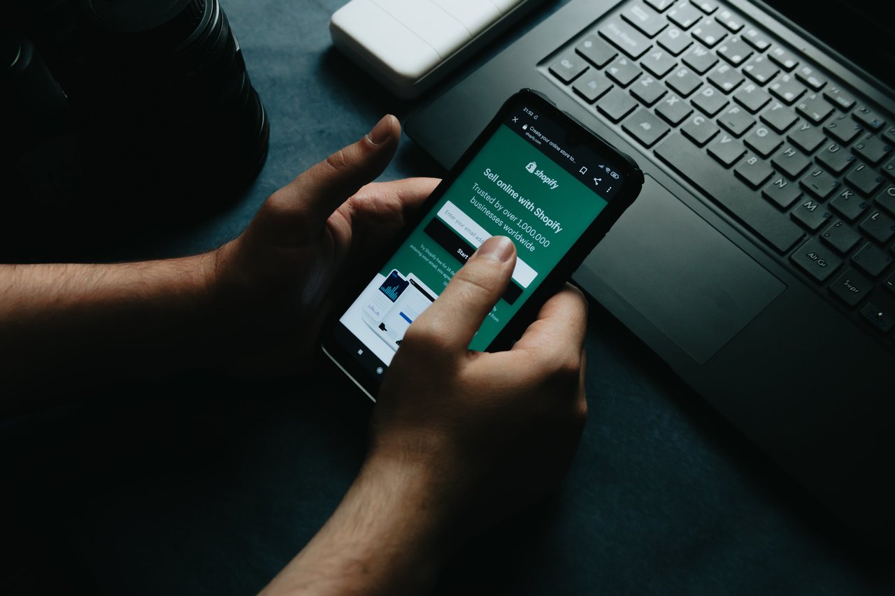 Shopify ana sayfasını gösteren cep telefonunu tutan eller