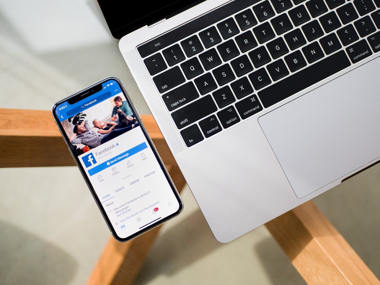 Facebook app on mobile phone next to MacBook showing social media marketing setup
