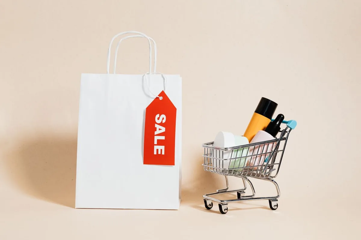 Shopping bag with a red SALE tag beside a small cart of products