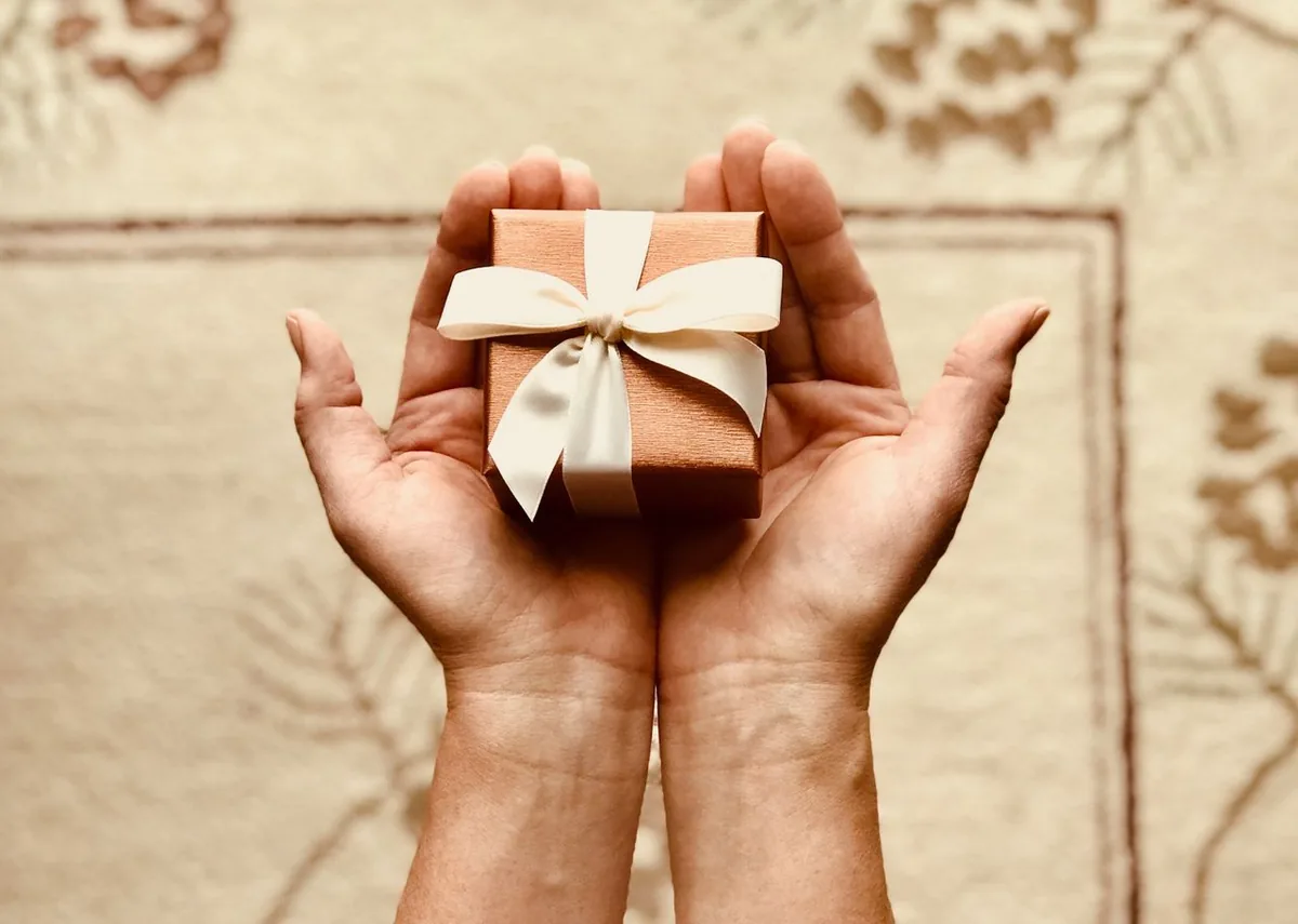 Hands holding a small gift box with a ribbon as a referral reward